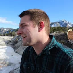Kyle West in a flannel shirt standing in front of Mammoth Springs, Yellowstone National Park.