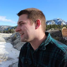 Image of Kyle West in a flannel shirt standing in front of Mammoth Springs, Yellowstone National Park.